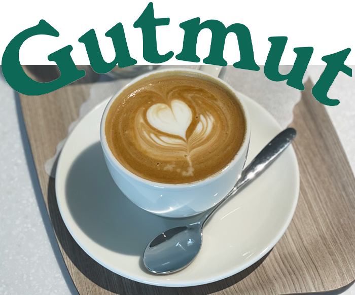 Das Foto zeigt einen Kaffee in einer weißen Tassen auf einem weißen Untersetzer mit einem Löffel