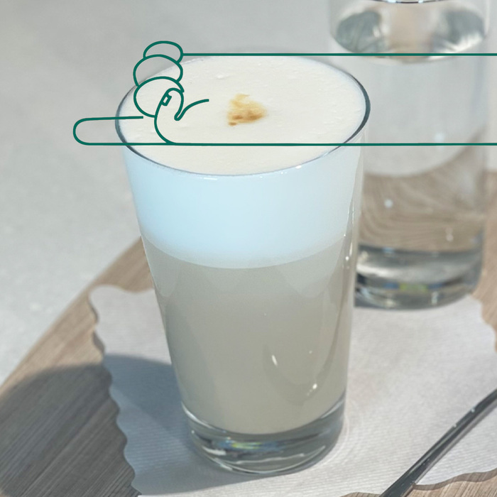 Das Foto zeigt eine Caffé Latte und darüber eine Illustration einer Hand die nach Links zeigt